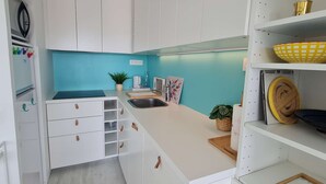 Una cocina compacta con gabinetes blancos, un muro azul de acento, un lavamanos y una pequeña isla con una planta.