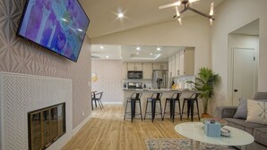 Una sala de estar moderna con chimenea, un televisor montado en la pared, una zona de cocina con taburetes de bar y una mesa de comedor.