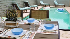 Mesa de comedor dispuesta con cuencos, platos y vasos azules, con vista a una piscina y sillas de descanso.