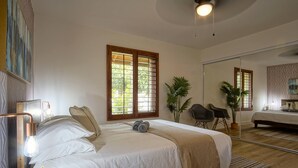 Un dormitorio bien iluminado con una cama grande, una mesita de noche con lámpara, un espejo y una planta en maceta.