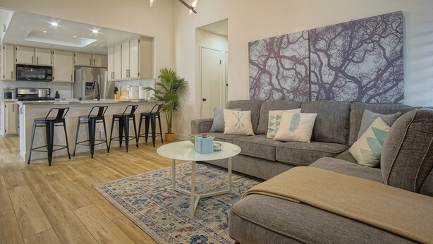 Una sala de estar moderna con un sofá gris, una mesa redonda para café y una zona de bar con taburetes.