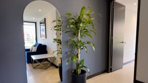 Ein modernes Interieur mit einem Blumentopf, einem Spiegel und Blick in einen Wohnbereich mit Sofa und Tisch.