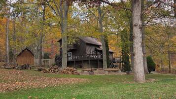 Un chalet rustique doté d’une terrasse, entouré d’arbres aux feuilles d’automne.