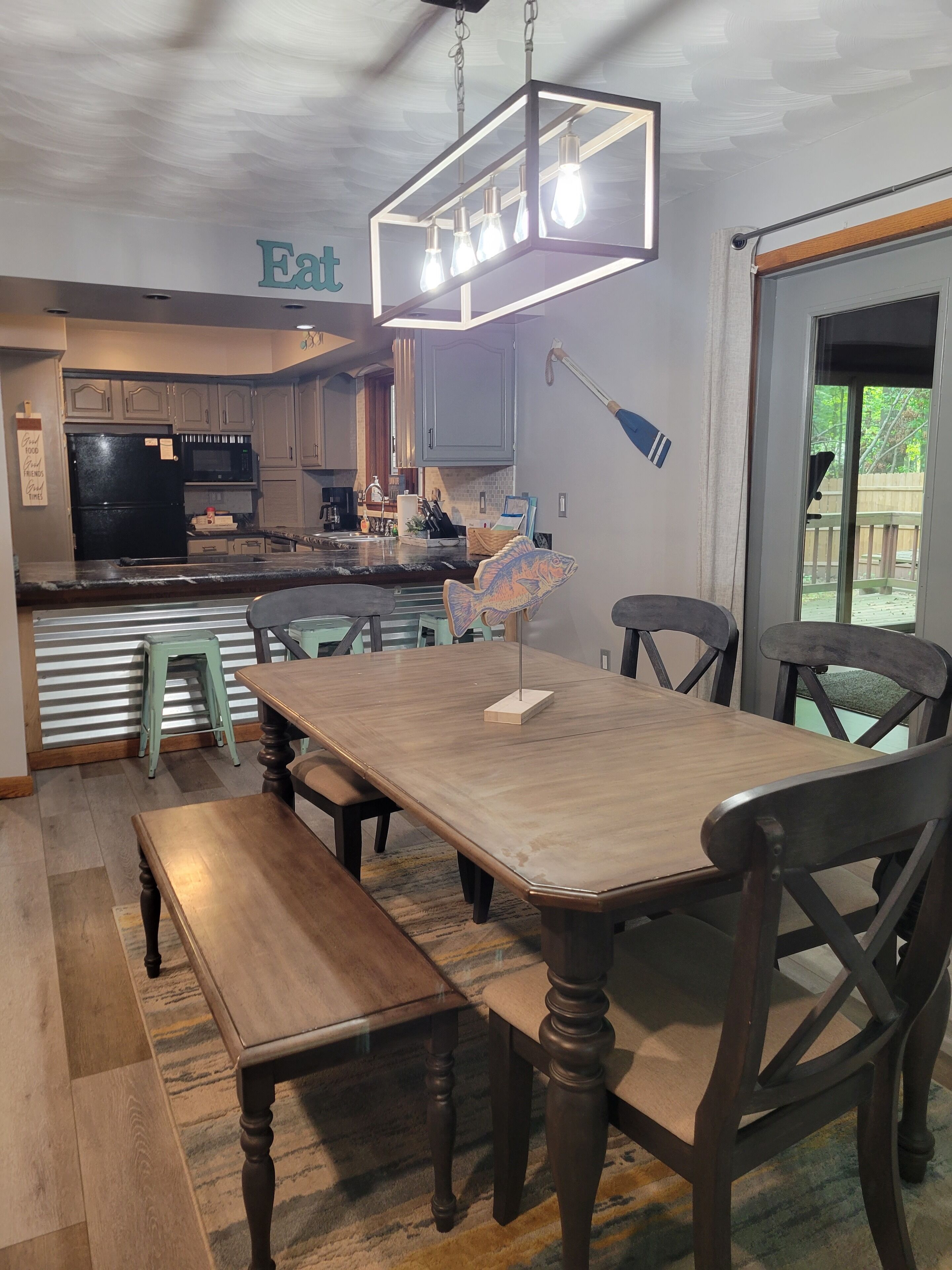 Une cuisine moderne dotée d’un îlot central, d’un coin repas avec une table et des chaises en bois, et offrant une vue sur l’extérieur grâce à une porte-fenêtre coulissante.