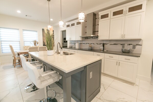 A modern kitchen with a large island, white cabinetry, and pendant lighting.