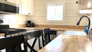 A modern kitchen with a wooden countertop, black chairs, a stove, and a window. - Cache Vista Tiny |Stunning Teton Views Cozy Retreat (Tetonia)