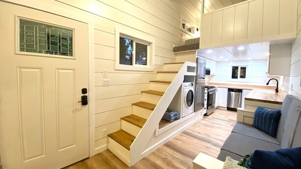 A compact, modern kitchen with built-in appliances, a wooden staircase, and a cozy seating area. - Cache Vista Tiny |Stunning Teton Views Cozy Retreat (Tetonia)