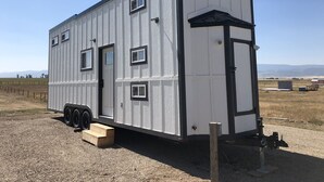A small, single-story metal building with a flat roof, a door, and multiple windows. - Cache Vista Tiny |Stunning Teton Views Cozy Retreat (Tetonia)