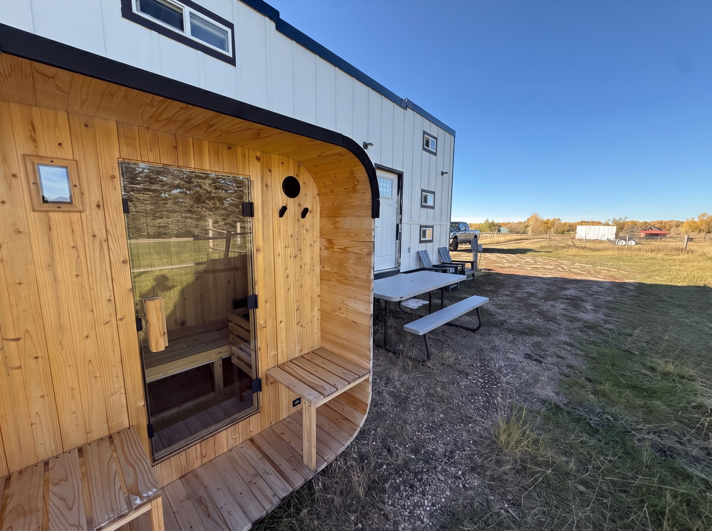 A wooden structure with a bench and a table, a vehicle in the background, and a clear sky.