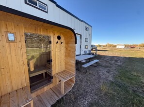 A wooden structure with a bench and a table, a vehicle in the background, and a clear sky. - Cache Vista Tiny |Stunning Teton Views Cozy Retreat (Tetonia)