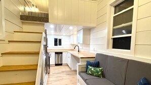 A compact kitchen with a built-in oven, a dining area with a wooden table, and a gray sofa with cushions. - Cache Vista Tiny |Stunning Teton Views Cozy Retreat (Tetonia)