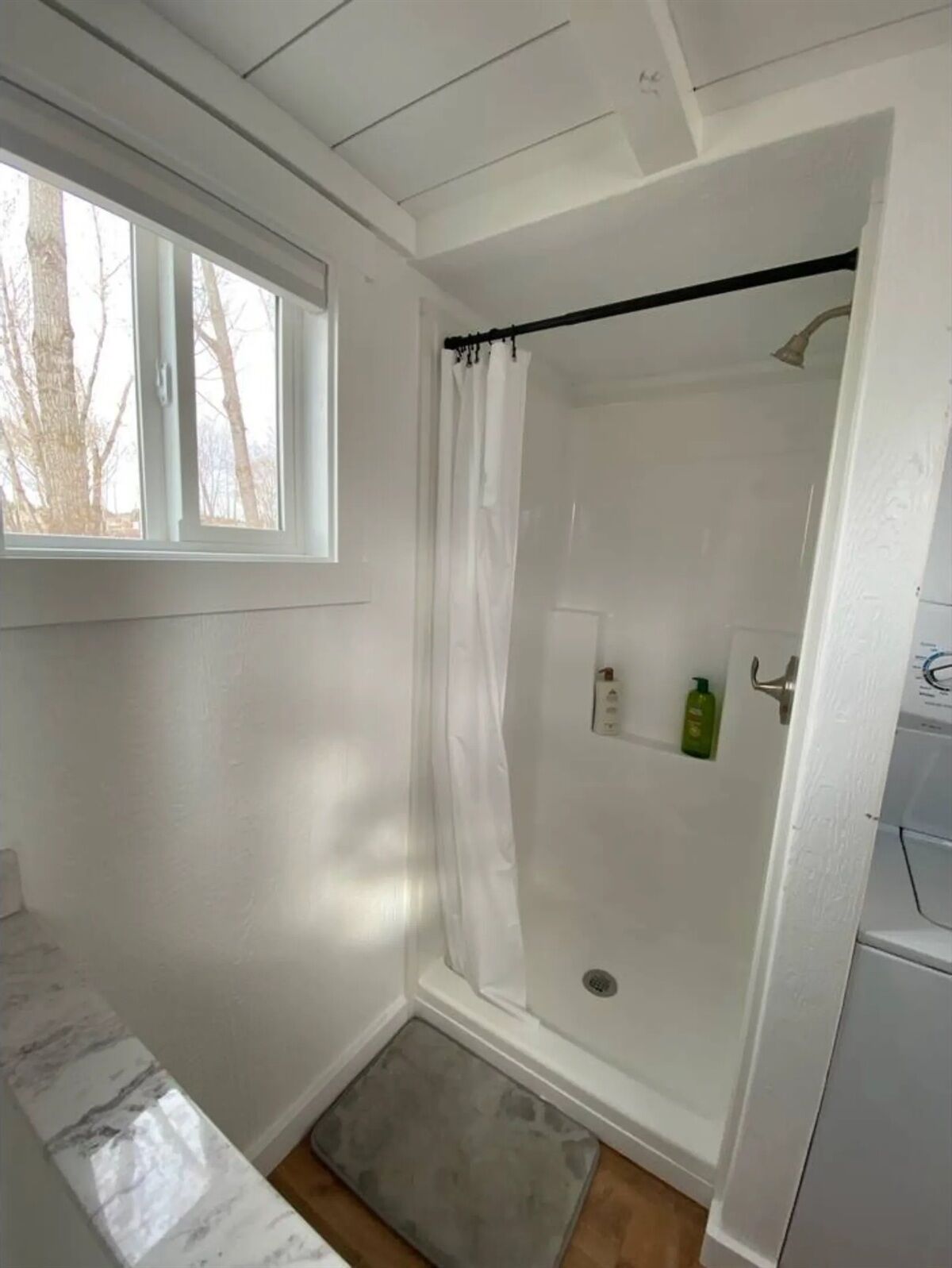 A shower with a glass door, a window above it, and a small shelf with toiletries.