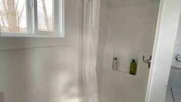 A shower with a glass door, a window above it, and a small shelf with toiletries.