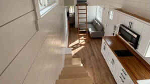 A narrow, multi-level interior with wooden floors, white walls, and a kitchen area with white cabinets and a wooden countertop. - Fall Rates- Stay Tiny, Dream Big~Tiny Timber House (Driggs)