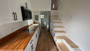 A modern kitchen with white cabinetry, a wooden countertop, and a built-in microwave. - Fall Rates- Stay Tiny, Dream Big~Tiny Timber House (Driggs)