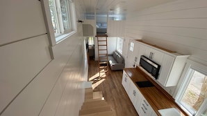 Un couloir étroit, au plancher en bois, qui mène à une chambre à coucher équipée d’un lit et d’une fenêtre.