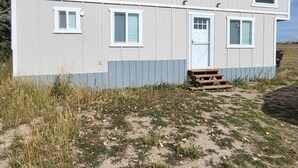 Il s’agit d’un bâtiment d’un seul étage, divisé en deux sections, doté d’un toit plat, de murs extérieurs blancs et d’un petit porche avec des marches menant à l’entrée.