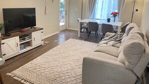 A living room with a TV, sofa, dining table, chairs, and a rug.