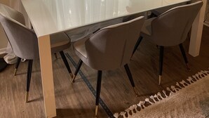 A dining area with a white table, grey chairs, a vase with red flowers, and a floor lamp.