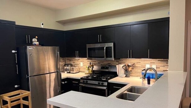 A modern kitchen with dark cabinets, stainless steel appliances, and a white countertop.