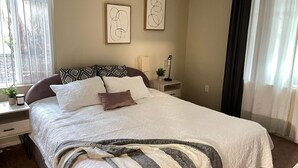A neatly made bed with a striped blanket, a bedside table with a lamp, and two framed artworks on the wall.