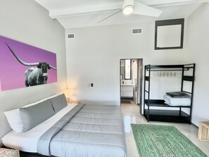 A bedroom with a bed, a bunk bed, a bathroom visible through an open door, and a ceiling fan. - Onyx Oasis: Modern 2/2 + Pool + Fire Pit + Hill Country Views + Minutes to Whitewater Amphitheater (Canyon Lake)