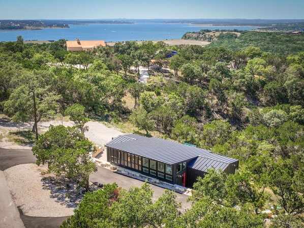 A modern house with a metal roof, surrounded by dense greenery and a clear view of the sea.