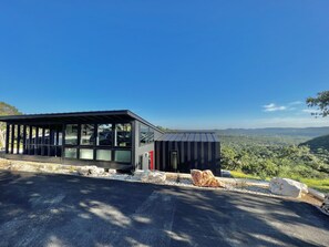 A modern building with large glass windows, a metal roof, and a view of a mountainous landscape. - Onyx Oasis: Modern 2/2 + Pool + Fire Pit + Hill Country Views + Minutes to Whitewater Amphitheater (Canyon Lake)