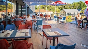 An outdoor dining area with tables and chairs, umbrellas, and a view of the surrounding buildings. - Près de la plage | Mobil-home | TV, Clim, Wifi (Saint-Hilaire-de-Riez)