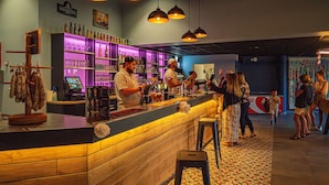 A bar with wooden counter, hanging pendant lights, and shelves stocked with bottles. - Près de la plage | Mobil-home | TV, Clim, Wifi (Saint-Hilaire-de-Riez)