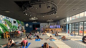 A spacious indoor area with multiple people performing yoga on mats, a bar area, and a mural with tropical designs. - Près de la plage | Mobil-home | TV, Clim, Wifi (Saint-Hilaire-de-Riez)