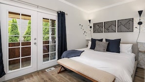 A bedroom with a bed, bench, and a view of greenery through a sliding door. - Spacious & Modern 3 Bedroom in Madison Valley (Seattle)