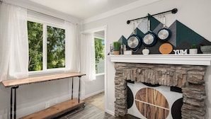 A room with a stone fireplace, a wooden bench, and a window with white curtains. - Spacious & Modern 3 Bedroom in Madison Valley (Seattle)