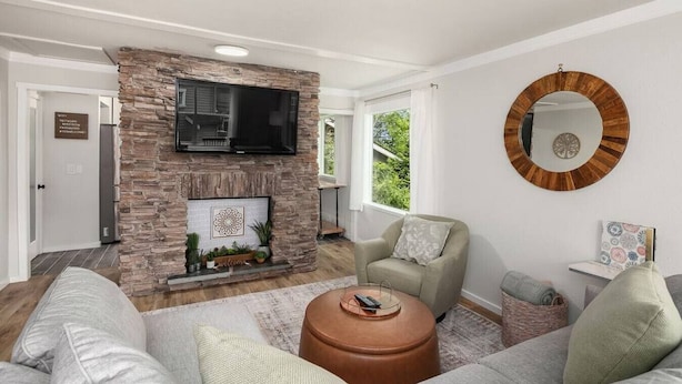A living room with a stone fireplace, a flat-screen TV, a round mirror, and a grey sofa with cushions. - Spacious & Modern 3 Bedroom in Madison Valley (Seattle)