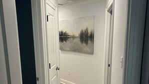 Käytävä, jossa on puulattia, valkoiset seinät ja maisemamaalaus.