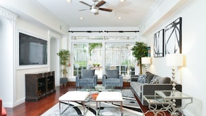 A spacious living room with a large TV, comfortable seating, and a ceiling fan.