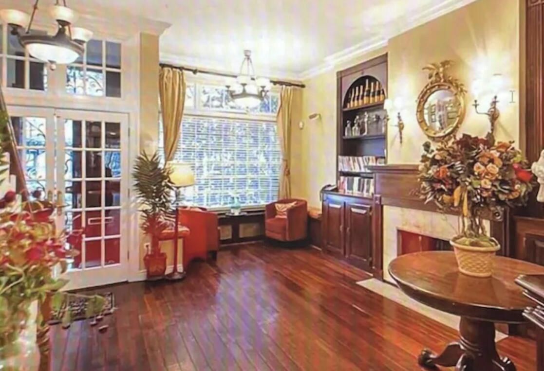 A room with wooden flooring, a fireplace, a bookshelf, and a window with curtains.