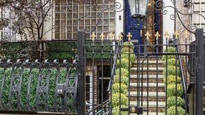 A gated entrance with a wrought iron fence, a blue door, and a stone staircase leading up to a building with a brick facade.