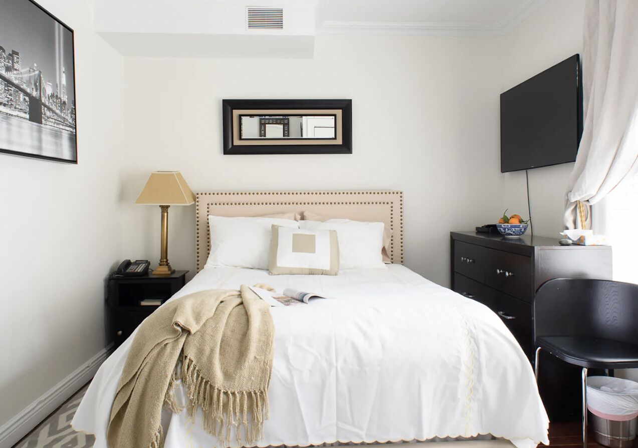 A neatly arranged hotel room with a bed, bedside table, lamp, and a flat-screen TV.
