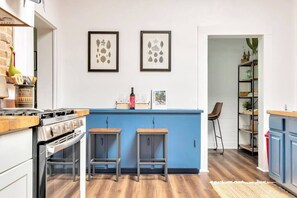 A kitchen with a blue island, two stools, a stove, and framed artwork on the wall.