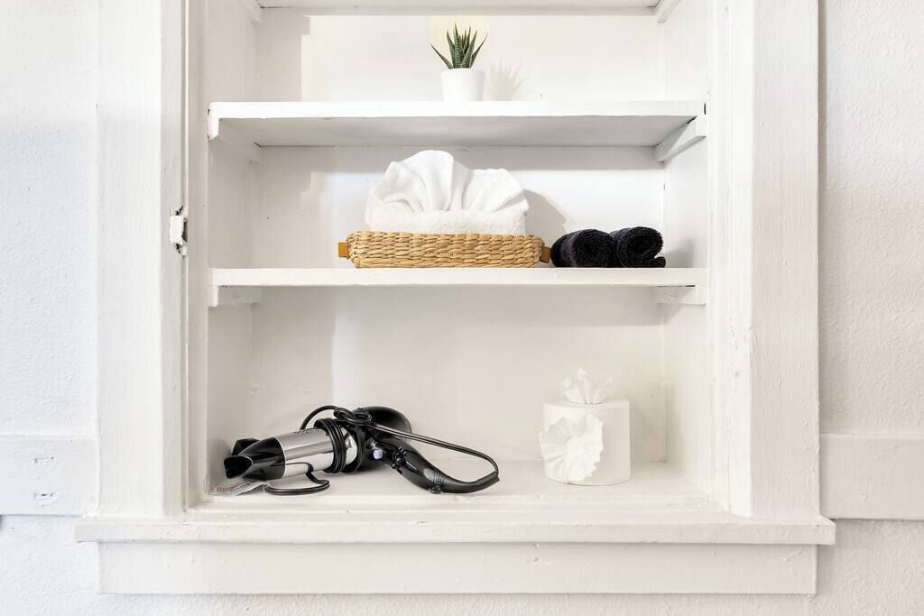 Ein weißer Schrank mit Regalen, der ein zusammenrolltes Handtuch, ein Paar Schuhe, eine kleine Topfpflanze, eine Taschentuchbox und eine Kamera enthält.