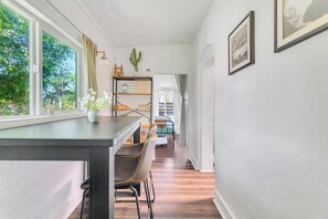 A modern interior with a dining area, a bookshelf, and a view of greenery outside.