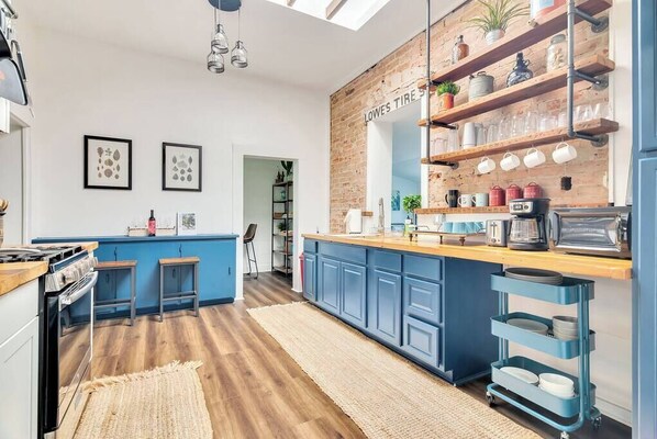 A modern kitchen with blue cabinets, a wooden countertop, and a brick accent wall.