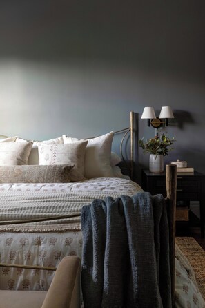 A bedroom with a bed, pillows, a bedside table with a lamp, and a plant.