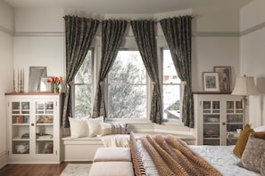 Um quarto acolhedor com uma grande janela, estantes embutidas e um espaço de estar confortável.