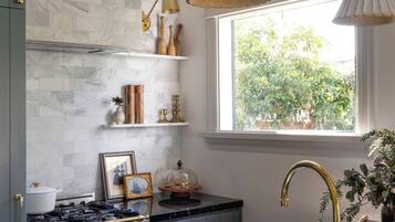 A modern kitchen with marble backsplash, a gas stove, a sink with gold fixtures, and a window with a view of greenery.