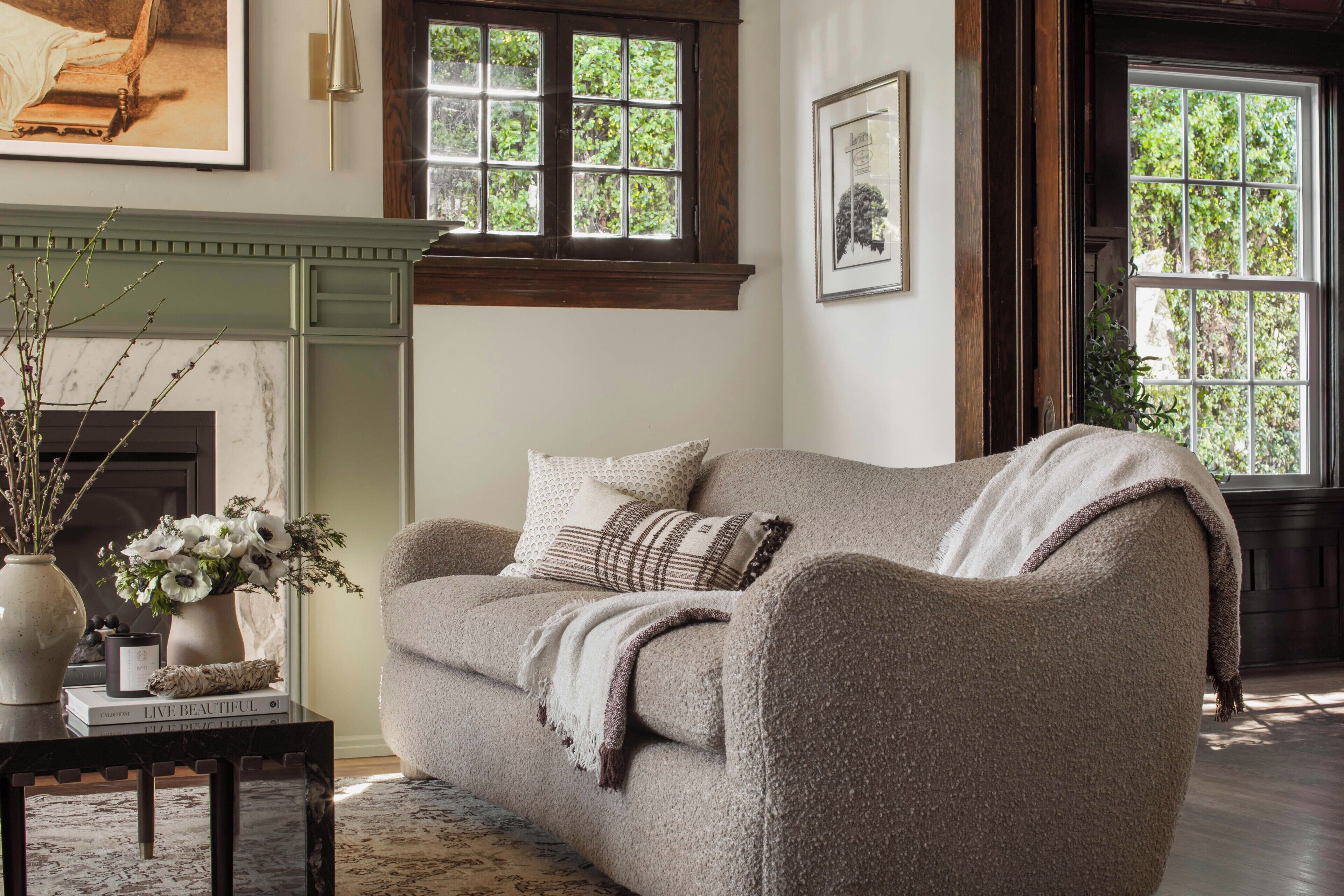 A cozy living room with a sofa, a fireplace, and a window with a view of greenery.