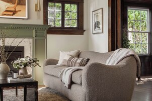 A cozy living room with a sofa, a fireplace, and a window with a view of greenery.