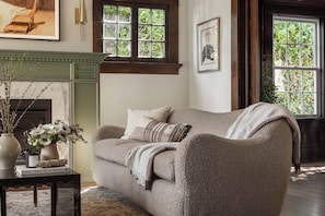 A cozy living room with a sofa, a fireplace, and a window with a view of greenery.