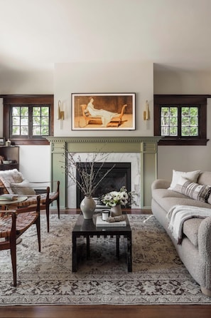A living room with a fireplace, a painting above it, and a sofa with a throw blanket. - The Craft House Inn (Santa Barbara)